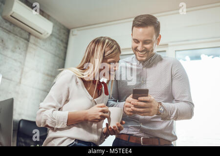 Les jeunes entrepreneurs souriant ayant pause café et à l'aide de smart phone au bureau. Banque D'Images
