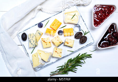 De petits morceaux de fromage brie, roquefort, camembert, cheddar et fromage aux noix sur une planche de bois blanc, vue du dessus Banque D'Images