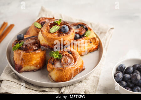 Brioches à la cannelle maison aux myrtilles et cannelle sur la plaque de fond gris, petit déjeuner Banque D'Images