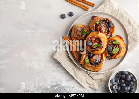 Brioches à la cannelle maison aux myrtilles et cannelle sur la plaque de fond gris, petit déjeuner Banque D'Images