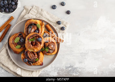 Brioches à la cannelle maison aux myrtilles et cannelle sur la plaque de fond gris, petit déjeuner Banque D'Images