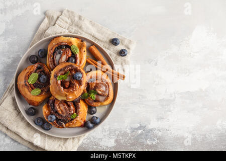 Brioches à la cannelle maison aux myrtilles et cannelle sur la plaque de fond gris, petit déjeuner Banque D'Images