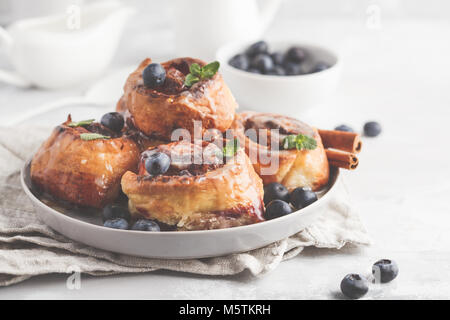 Brioches à la cannelle maison aux myrtilles et cannelle sur la plaque de fond gris, petit déjeuner Banque D'Images