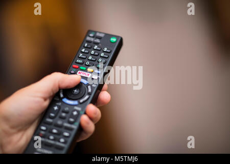 Une personne à l'aide d'un téléviseur avec télécommande un logo Netflix sur le bouton - Février 2018 Banque D'Images