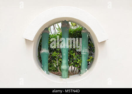 Trou rond - fenêtre dans mur blanc du jardin public au monastère bouddhiste, Penang, Malaisie Banque D'Images