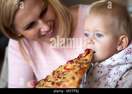 Petite fille mange une grande tranche de pizza à partir de sa mère. Children's pizza. Banque D'Images