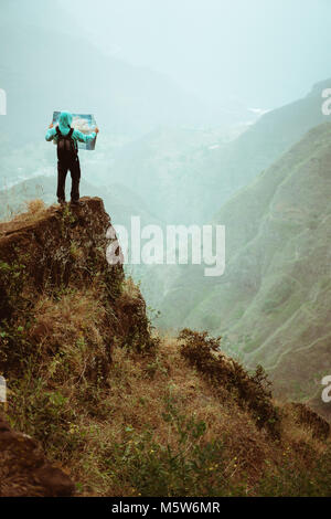 Seul randonneur avec carte de l'île d'un séjour sur une barre rocheuse en face d'une magnifique vue panoramique de hautes chaînes de montagne et vallée verdoyante. Santo Antao Cape Verde Banque D'Images