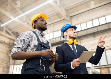 Low angle view of handsome inspecteur barbu wearing hardhat et costume classique d'effectuer une inspection dans le département de production de l'usine moderne, Afri Banque D'Images