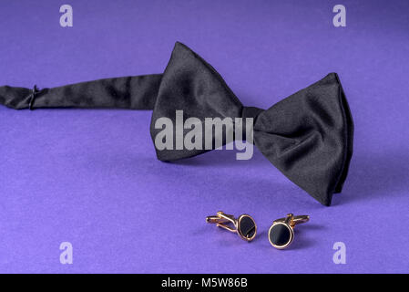 Noeud papillon noir avec boutons de manchette sur fond violet. Banque D'Images
