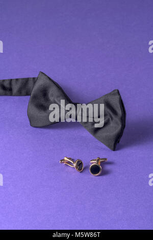Noeud papillon noir avec boutons de manchette sur fond violet. Banque D'Images