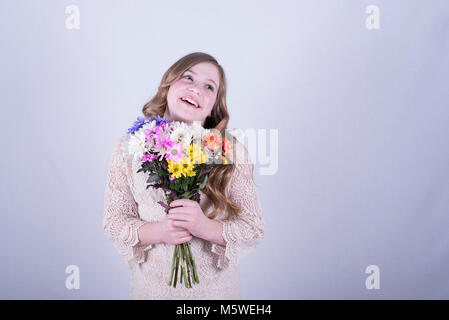 12-year-old fille avec de longs cheveux blond sale, bouquet de marguerites colorées holding smiling, looking up et sur le côté, fond blanc Banque D'Images