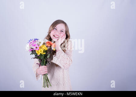 12-year-old fille avec de longs cheveux blond sale, holding bouquet de marguerites colorées, à rire, une main sur le côté du visage, yeux ouverts, fond blanc Banque D'Images