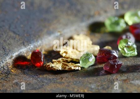 Uncut rouge vert et des péridots, grenats pépites d'or de Laponie, affichée sur un rusty gold pan Banque D'Images