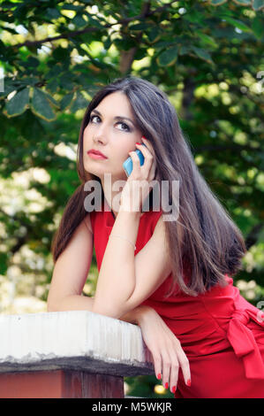 La jeune fille dans une robe rouge sur la rue parle par téléphone Banque D'Images