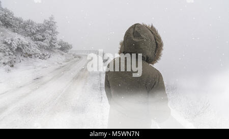 Scène d'hiver avec de la neige et de la femme près de la route. Arrière de la figure féminine en hiver avec une capuche coupe-vent debout sur un pic de montagne quand il neige. Banque D'Images