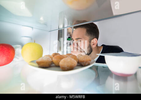 Close-up of a Young Man Holding son nez près de mauvais aliments dans réfrigérateur Banque D'Images