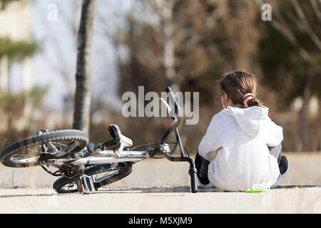 10-year-old girl sitting d'épées dans l'appareil photo en train de déjeuner avec son vélo. Coup horizontal avec lumière naturelle Banque D'Images