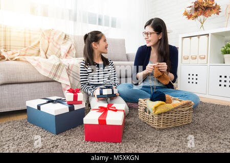 Asiatique charme mère et sa fille tricotant ensemble pour la maison de vacances avec plusieurs boîtes cadeaux même assis sur marbre de la salle de séjour à la maison. Banque D'Images