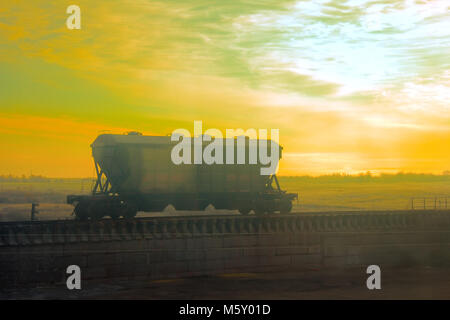 L'auto décharger des cargaisons de vrac le transport de wagons (wagons de ballast ; hopper-doseur) sur fond de ciel de coucher du soleil. Pour la publicité du transport ferroviaire Banque D'Images