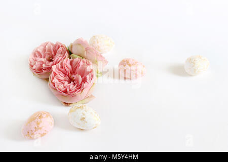 Carte de vœux, d'invitation de printemps. Les oeufs de Pâques rose et blanc avec des taches d'or et rose fleurs couché sur le tableau blanc. Style Féminin stock photo, composition florale. Banque D'Images