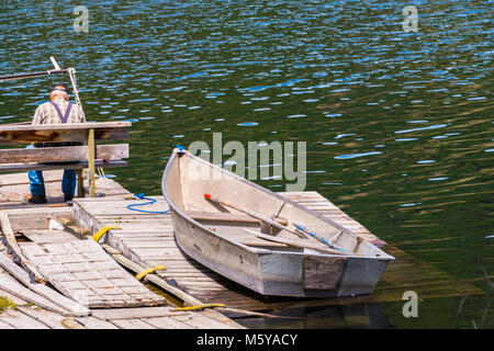 Old Wooden Row Boat Dock avec le vieil homme assis sur un banc et la pêche . Copier l'espace. Banque D'Images