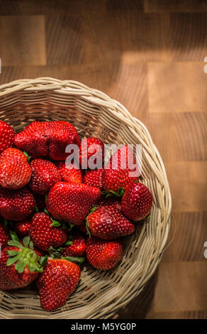Le rouge fraise mûre dans panier en osier sur un bureau en bois. Banque D'Images