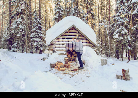 Homme couper du bois dans la forêt près de la cabane. Jour d'hiver glacial. Banque D'Images