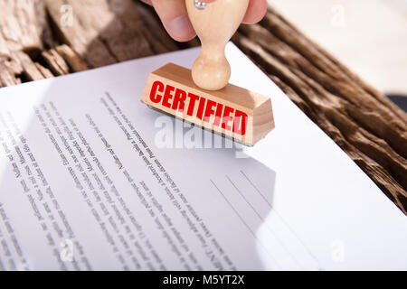 Close-up of a person holding timbre certifié sur le document sur un bureau en bois Banque D'Images