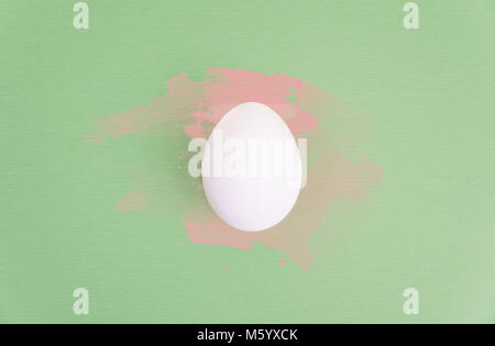 L'un des oeufs blancs sur fond vert pastel aquarelle rose avec des éclaboussures. Banque D'Images