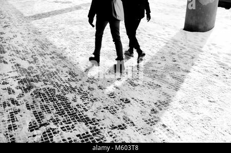 Les jambes de deux personnes marchant sur le trottoir enneigé en mouvement blurin noir et blanc Banque D'Images