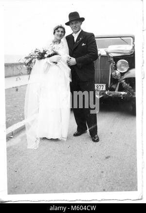 Années 1960 Années 1970 wedding couple looking at camera posant devant une vieille voiture. Tourné en noir et blanc. Italie Banque D'Images