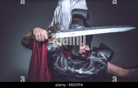 Lutteur, gladiateur romain et guerrier de Rome avec casque et manteau rouge, porte une épée de fer, barbe et cheveux longs. Banque D'Images