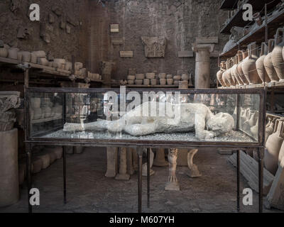 Corps d'une exposition d'une victime de Pompéi dans un boîtier en verre, avec d'autres objets excavés. Pompéi. Italie. Banque D'Images