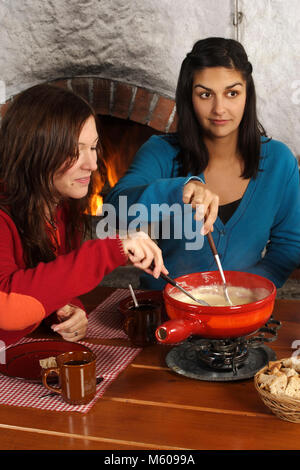 Photo de deux belles femmes trempant dans le pain de fromage fondu dans un caquelon. L'accent est sur la fille de gauche. Banque D'Images