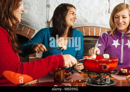 Photo de trois belles femmes trempant le pain dans le fromage fondu dans un caquelon. Banque D'Images