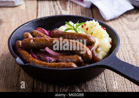 Casserole de saucisse et l'oignon servi avec purée de pomme de terre de la poêle en fonte sur table en bois rustique Banque D'Images