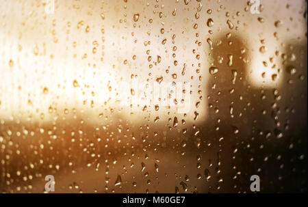 L'eau de pluie sur une vitre, avec une ville de l'arrière-plan, des tons chauds de jaune et orange au coucher du soleil filtre couleur Banque D'Images