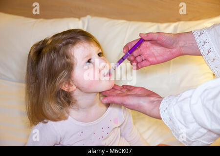 Mère / mère / mère donnant Calpol médicament avec du paracétamol pour - apparemment - un malade / enfant malade / enfant / fille au lit avec de la fièvre ou de la température. (95) Banque D'Images