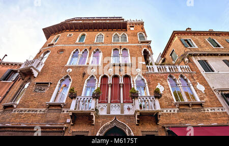 Vue l'heure avancée de bas en vieille brique façade richement décorée d'un immeuble avec balcon. Ciel nuageux bleu vif sur l'arrière-plan. Venise, Italie Banque D'Images