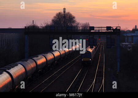 Une huile DB Cargo train passe un Crosscountry Birmingham - Nottingham Nottingham extérieur service station avec le coucher du soleil étincelant sur le train de marchandises Banque D'Images