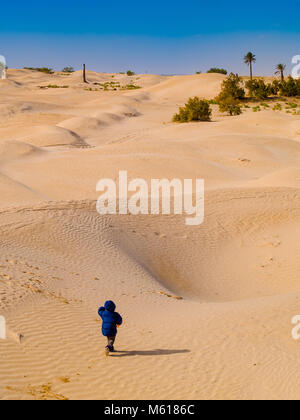 Dans le désert du Sahara, l'enfant joue avec le sable des dunes, en vacances, tourisme Tunisie Douz Banque D'Images