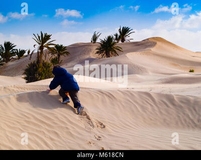 Dans le désert du Sahara, l'enfant joue avec le sable des dunes, en vacances, tourisme Tunisie Douz Banque D'Images