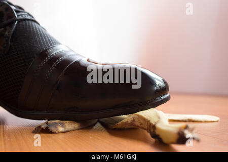 Chaussure noir du jeune homme glissa sur une peau de banane. Banque D'Images