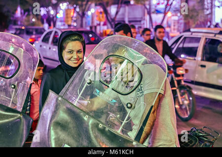 Kashan, Iran - avril 25, 2017 : famille iranienne dans un parking dans la soirée, une femme dans un hijab est souriant, c'est l'homme à la moto par un gl Banque D'Images