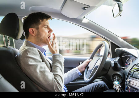 Vue latérale d'un jeune homme de bâiller pendant la conduite Voiture Banque D'Images