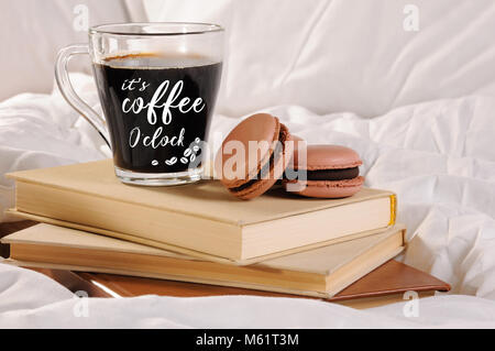 Tasse de café du matin avec les gâteaux au chocolat macarons, sur une pile de livres dans le lit. L'inscription sur la coupe est "c'est le café o'clock" Banque D'Images