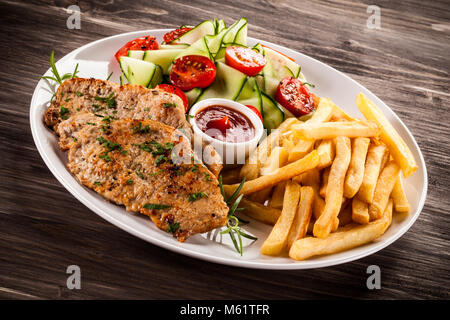 Côtelette de porc frit, des pommes de terre et légumes grillés sur table en bois Banque D'Images