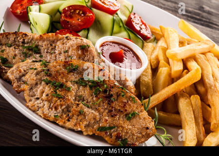 Côtelette de porc frit, des pommes de terre et légumes grillés sur table en bois Banque D'Images