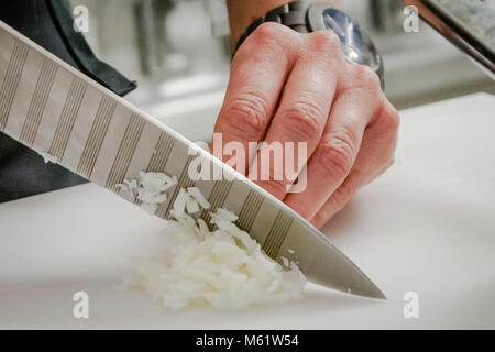 Cuisine travail hacher des onions. Pour que vous n'ayez pas envie de pleurer, voici un conseil du sous-chef : respirez par la bouche lorsque vous épluchez et hachez des oignons. Un couteau tranchant est également très important - par exemple, le Chroma P 30 dans le design Porsche. Banque D'Images