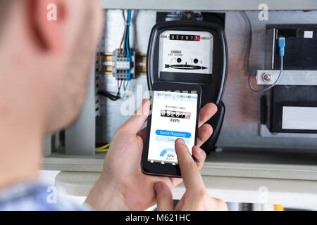 Close-up of a Man's Hand Holding Mobile Phone Lecture compteur électrique Banque D'Images